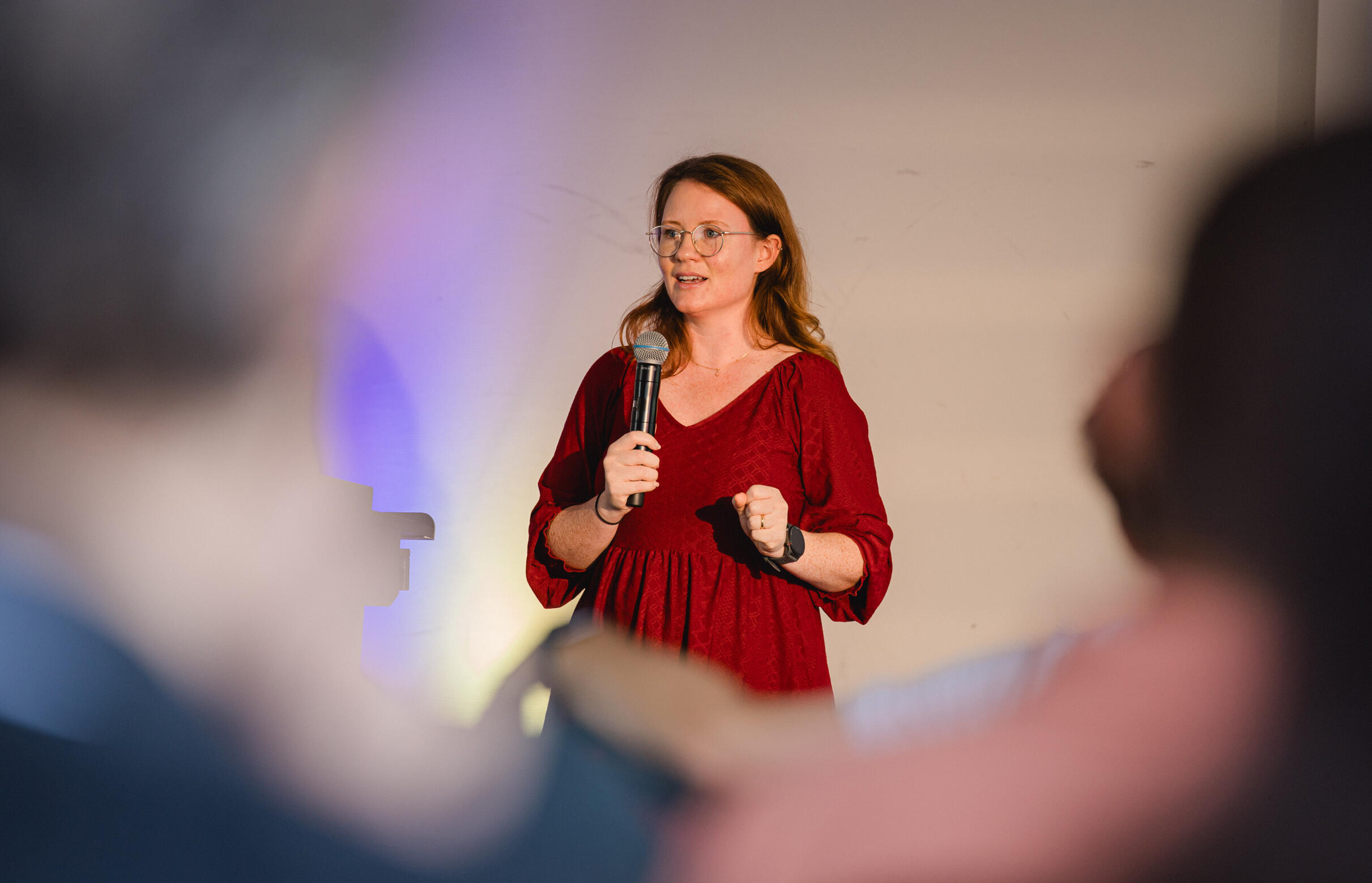 Photo of Robin giving a presentation pointing to a slide with code, with a microphone in her hand